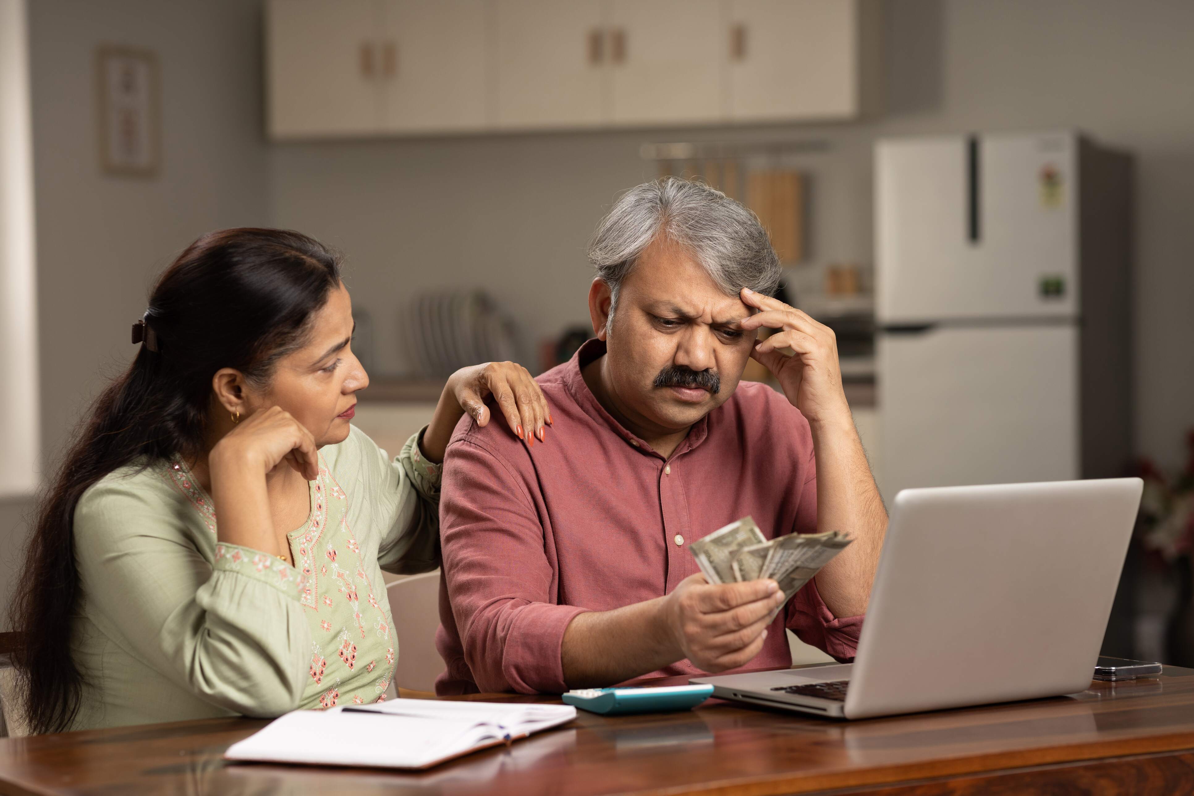 Worried mature couple counting money at white using laptop indoors Image